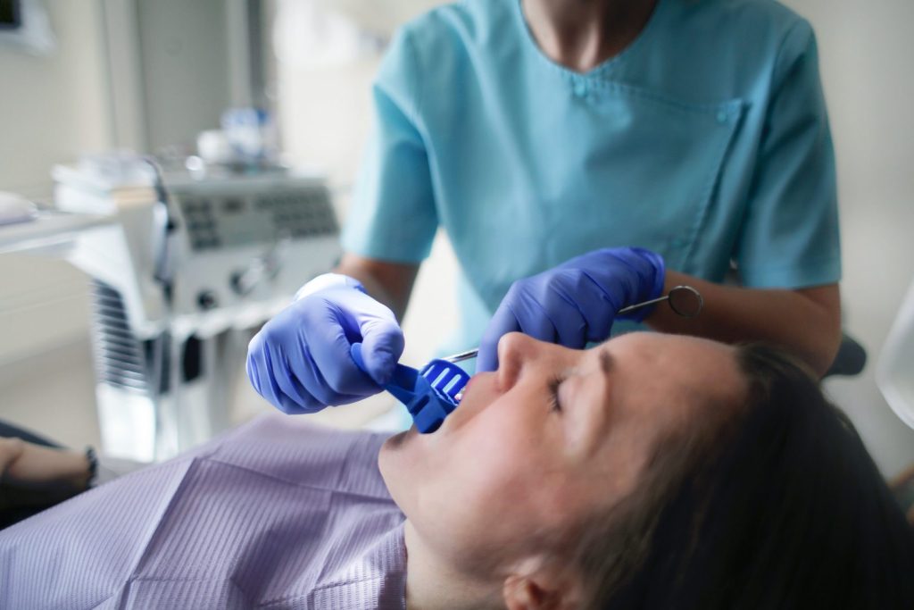 Dental assistant in scrubs placing a fluoride tray into a patient's mouth