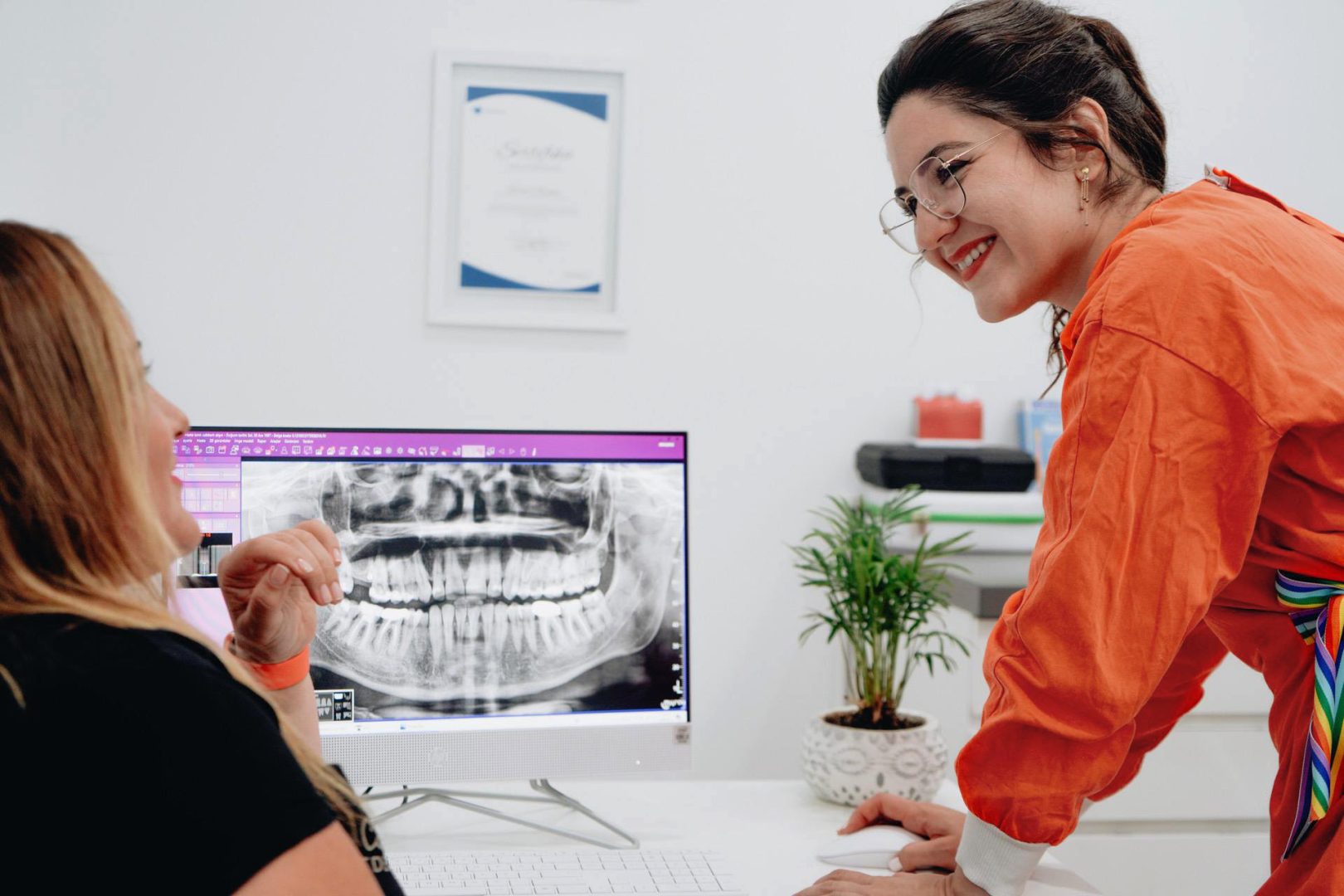 Dental assistant smiling at patient and showing x-rays on computer