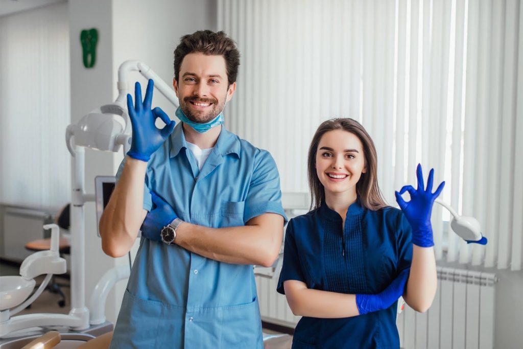 Dentist with assistant smiling and showing the okay sign.