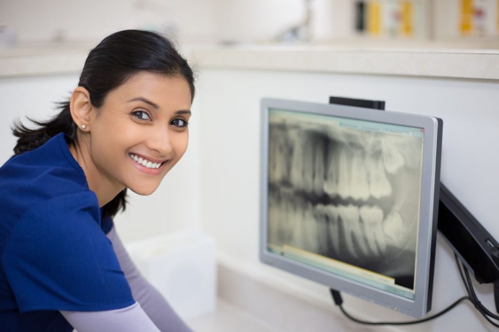 Smiling dental assistant with xray on computer screen