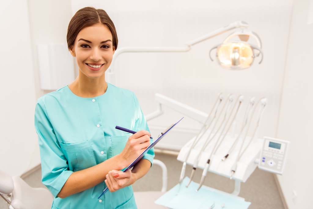 Dental assistant smiling with clipboard in exam room