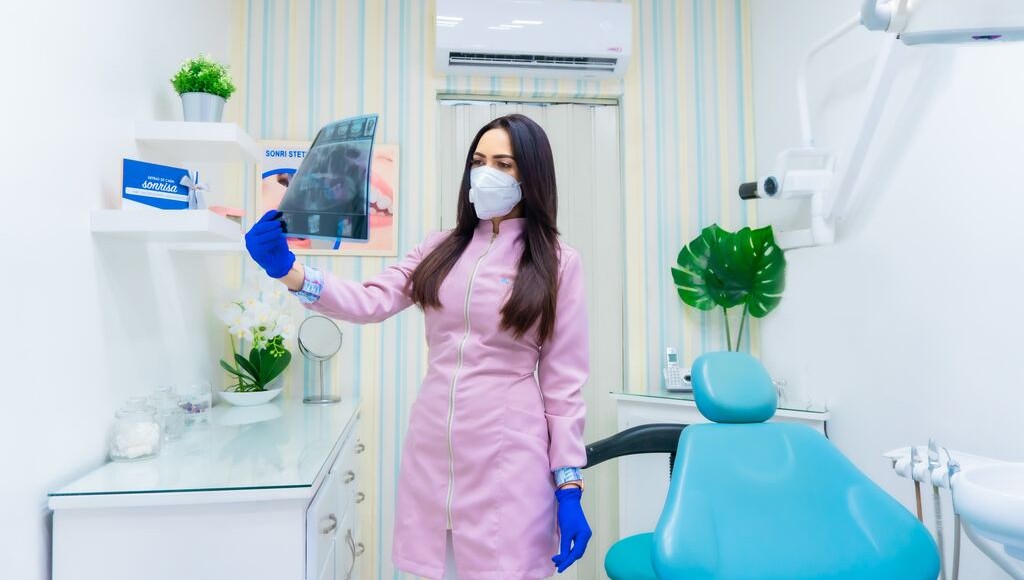 examining xrays, pink coat, blue chair, white room, striped wall paper, green plants