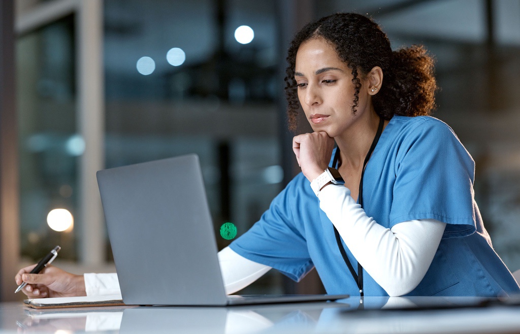 Woman in scrubs learning online at laptop at night