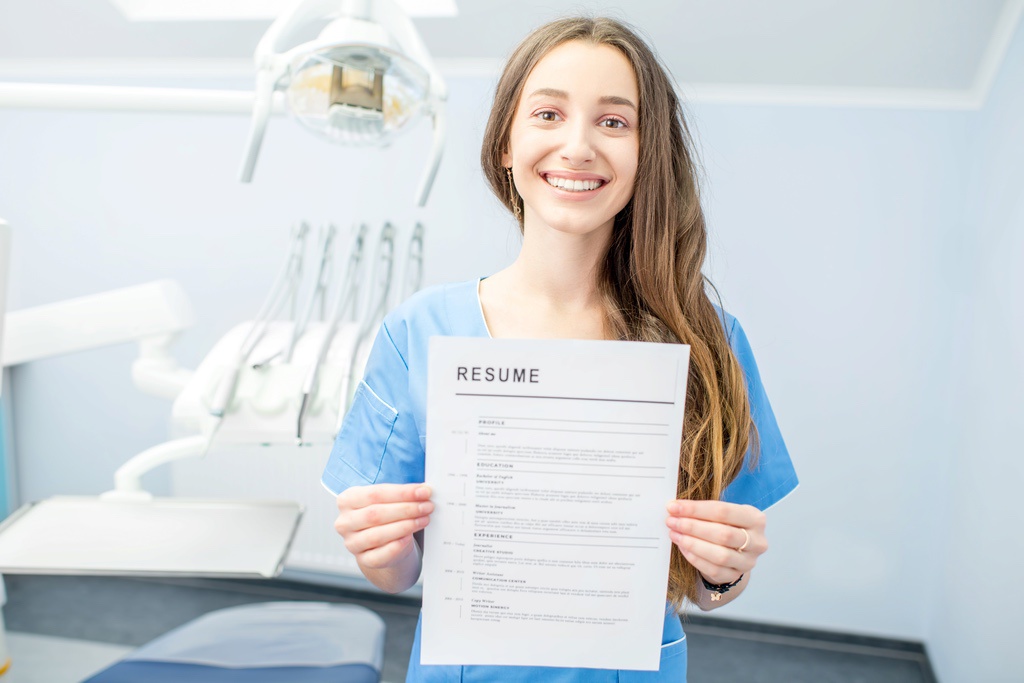 Smiling dental assistant holding up resume in exam room