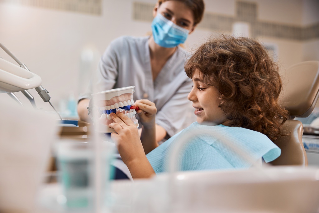 Dental assistant educating young patient about brushing teeth with model to illustrate relevant skills to include on resume