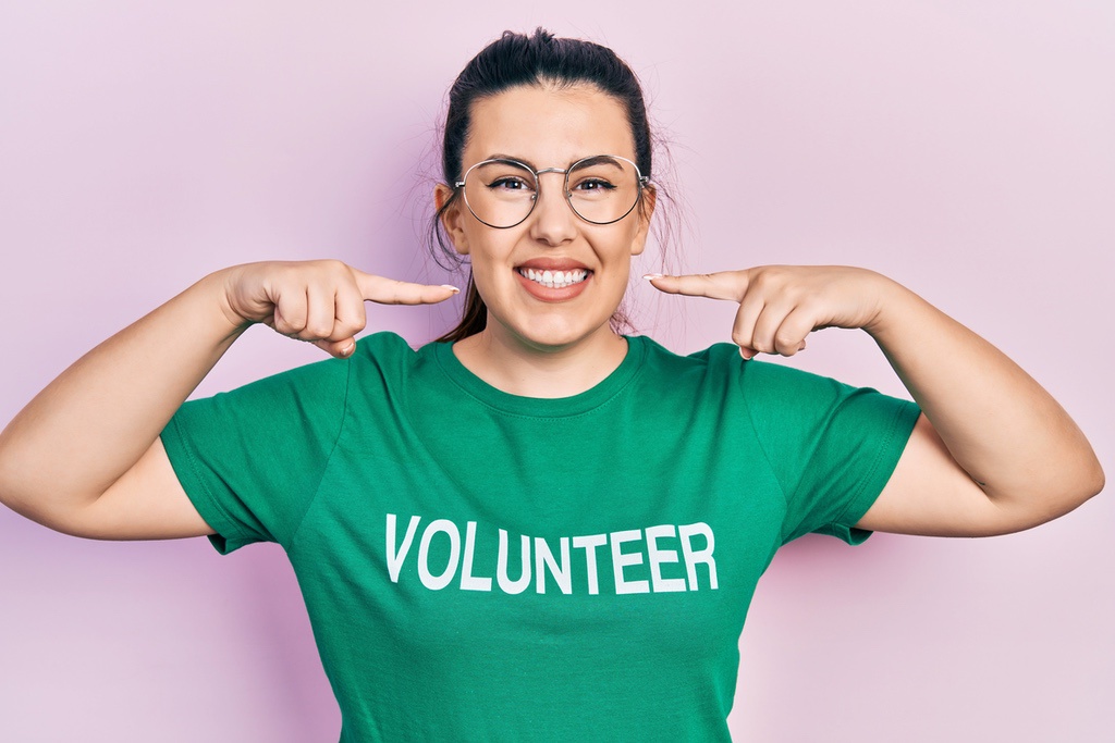 Dental assistant in volunteer shirt pointing to smile to symbolize importance of highlighting volunteer experience