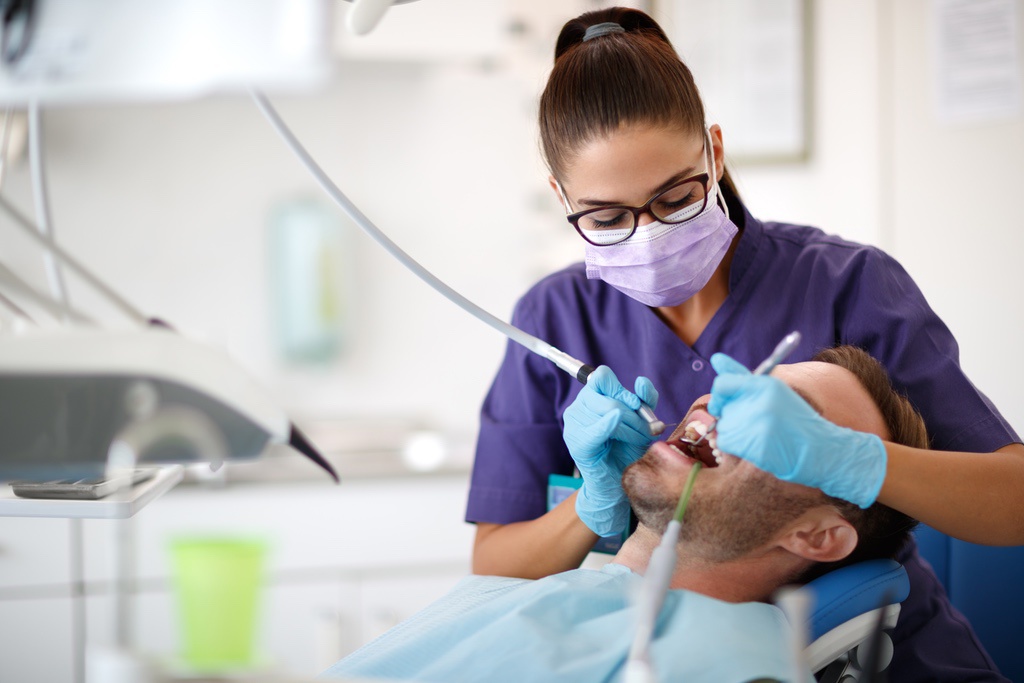 Dental assistant polishing patient's teeth in practice