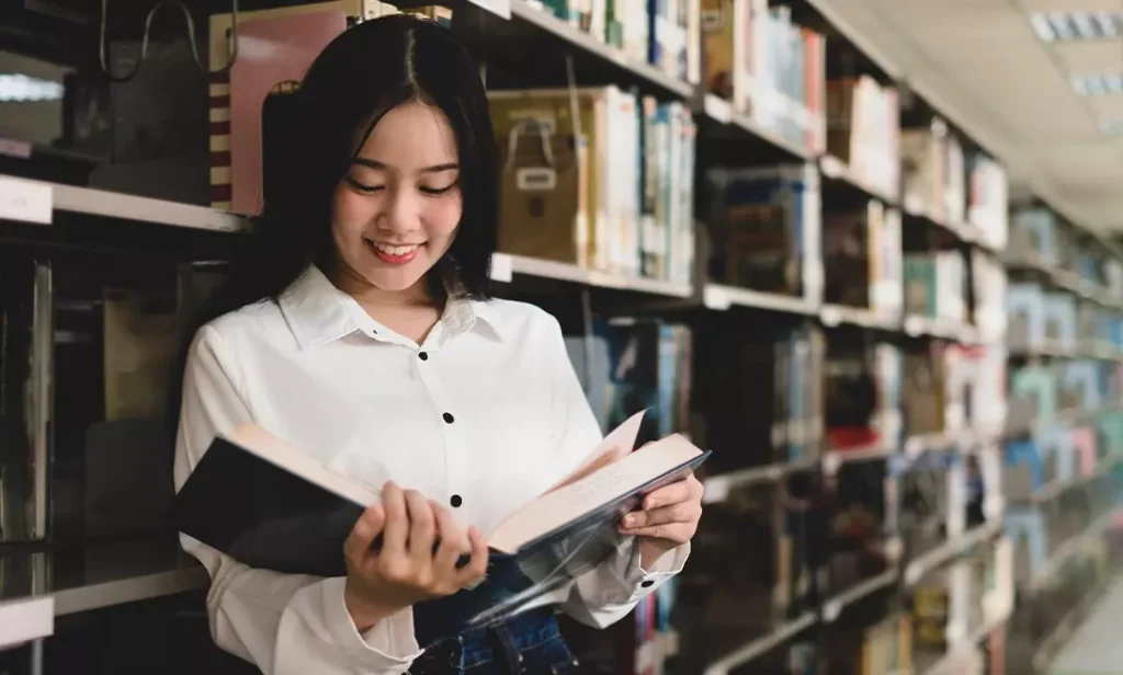 Female dental assistant student standing in library reading textbook