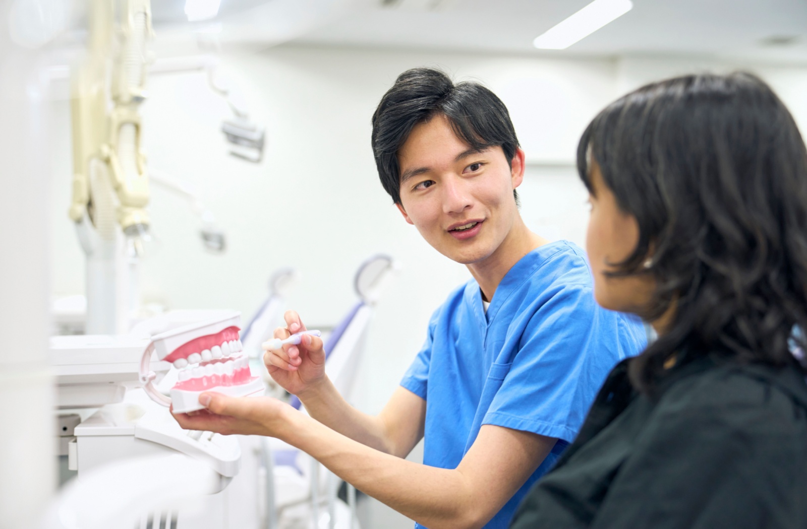 dental-assistant-demonstrating-oral-care Two dental students having a discussion in a clinic, with a pair of fake teeth.