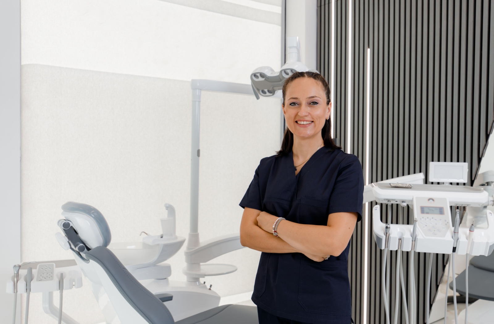 dental-assistant-smiling-in-dental-office A dental assistant smiling with their arms crossed in the exam room.