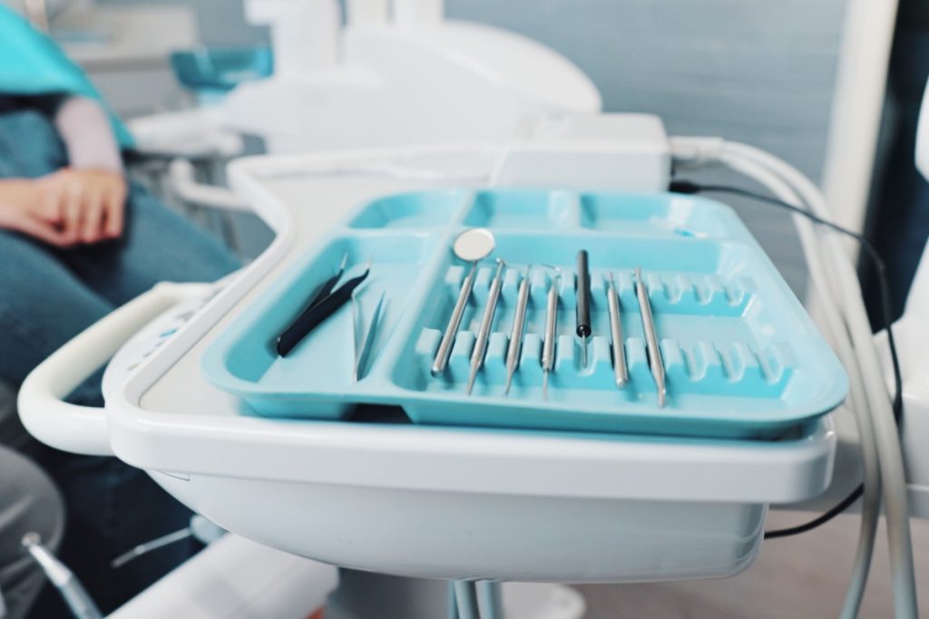 A tray of clean dental instruments neatly arranged beside a patient seated in a dental chair.